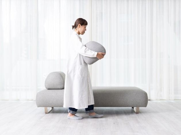 Reposの背クッションを持った人が画面左から中央に向かって歩く